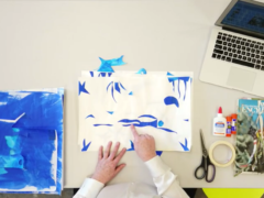 A still image from ART RECESS video. Overhead image of hands creating a blue and white collage on a table with art supplies and a laptop nearby,