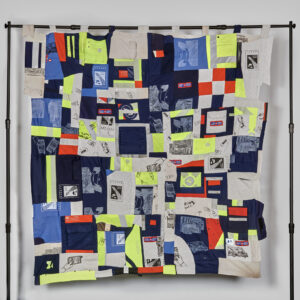 A patchwork quilt hanging on a simple black metal structure. The quilt is made out of pieces of Canada Post letter carrier uniform.